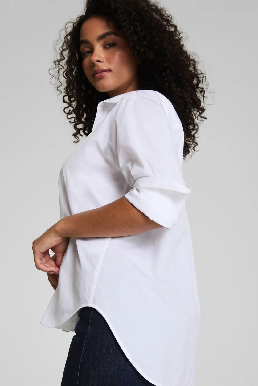 Woman wearing a white blouse with rolled-up sleeves on a plain background