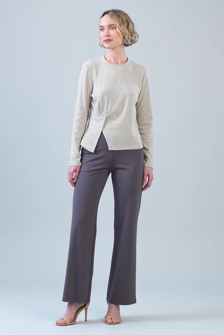 A woman modeling a light beige knit wrap-style cardigan and dark gray wide-leg trousers against a light gray studio background.