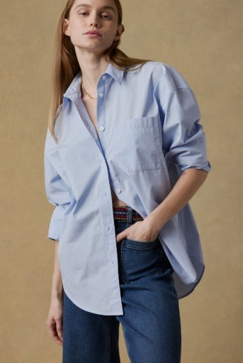 Woman wearing a light blue shirt and dark jeans against a beige background