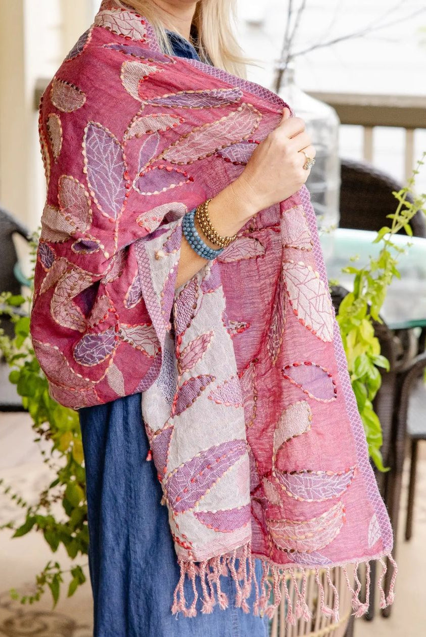 A woman on a balcony wearing a pink and lavender leaf-patterned shawl with fringe, paired with a blue dress.