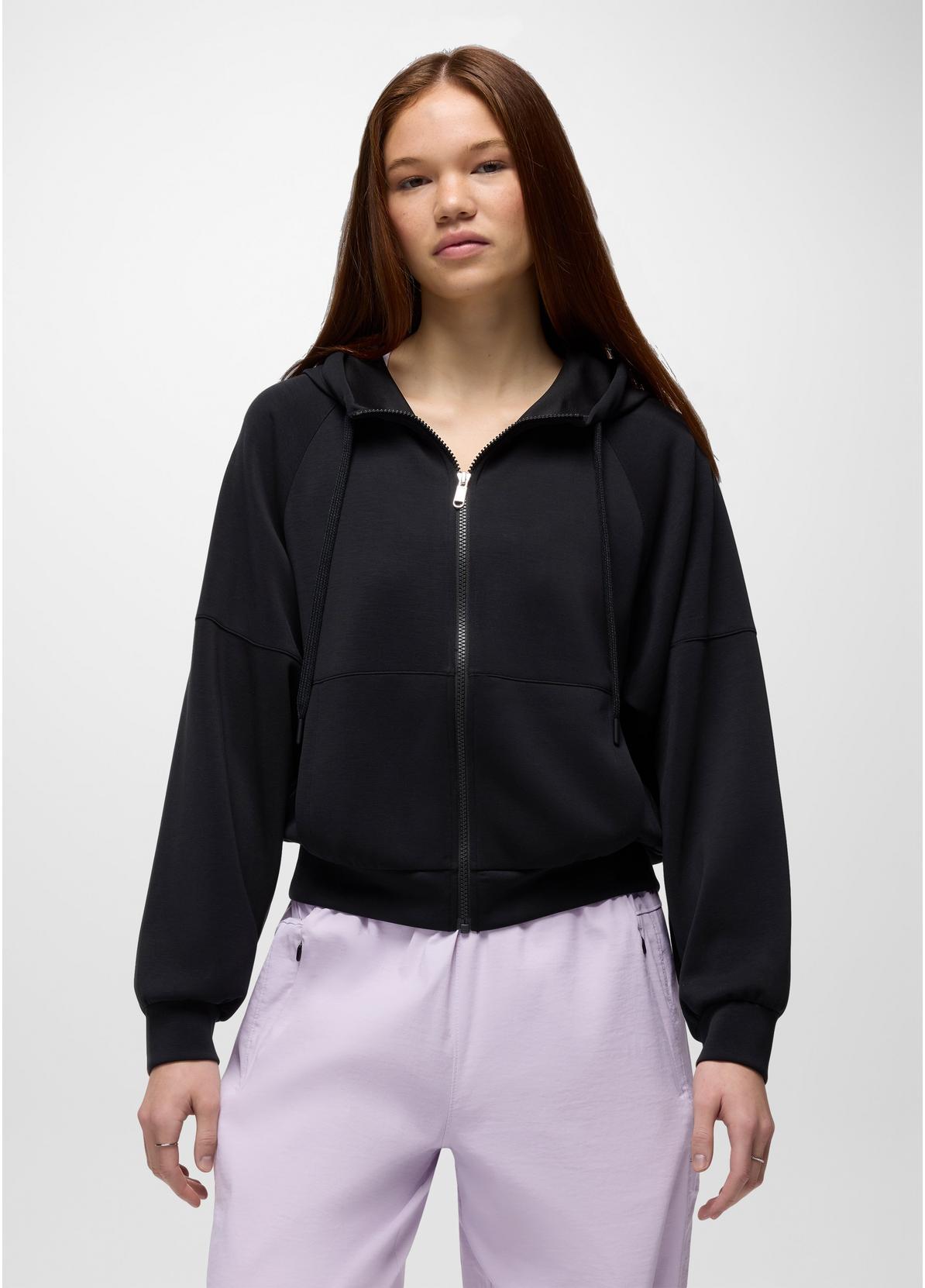Person wearing a black zip-up hoodie and light purple pants on a white background