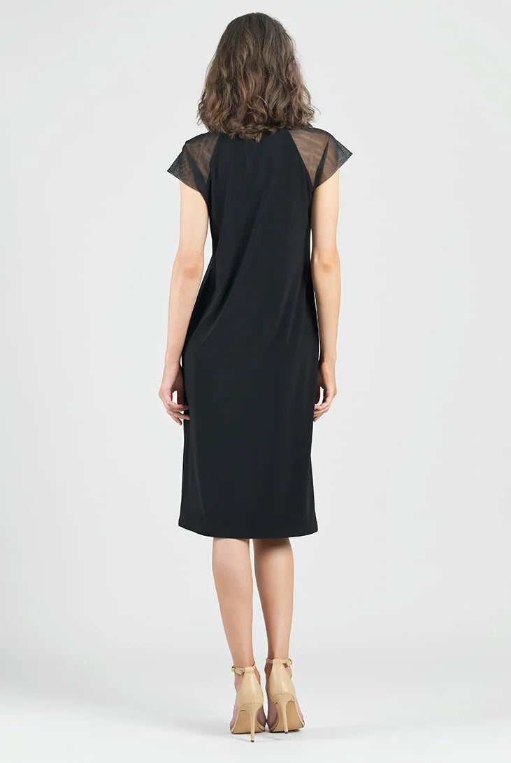 A woman viewed from behind wearing a black knee-length dress with sheer mesh cap sleeves, paired with beige high-heeled sandals, against a light gray studio background.
