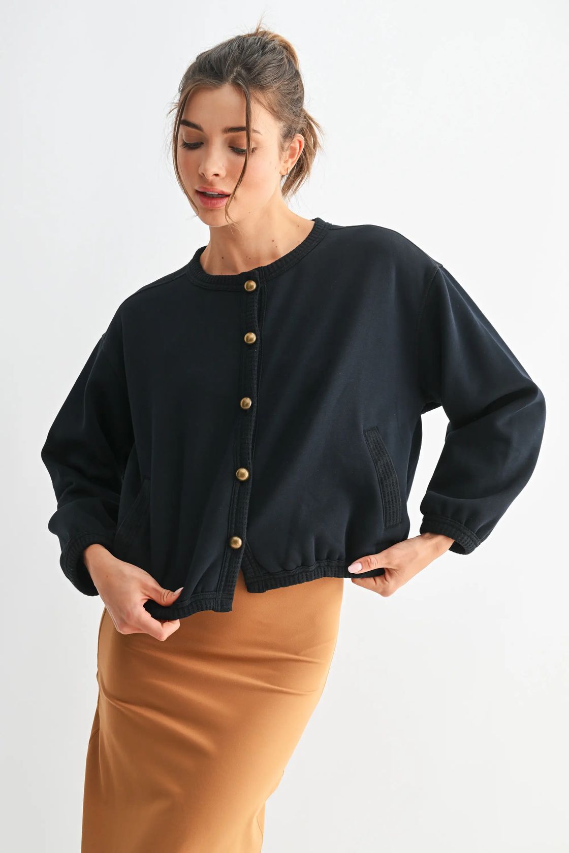 Woman wearing a black cardigan with gold buttons on a white background