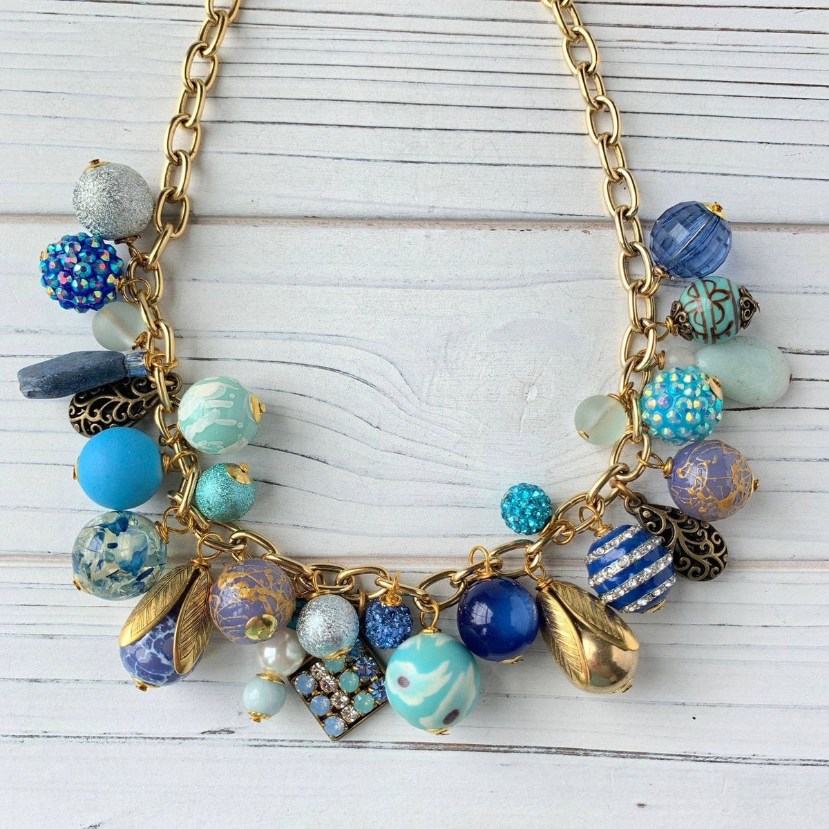 Sail Away Charm necklace, colorful beaded charm necklace with gold chain, blue and gold beads and charms, shown on a light wooden surface