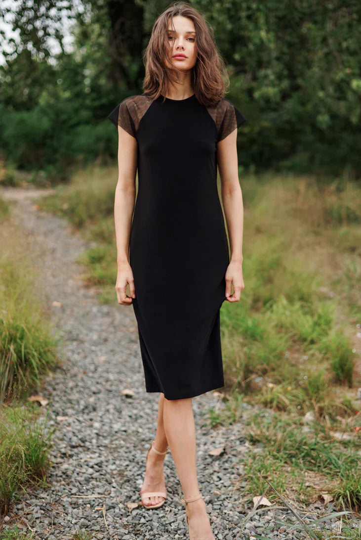 Woman in a black dress standing on a gravel path with greenery around