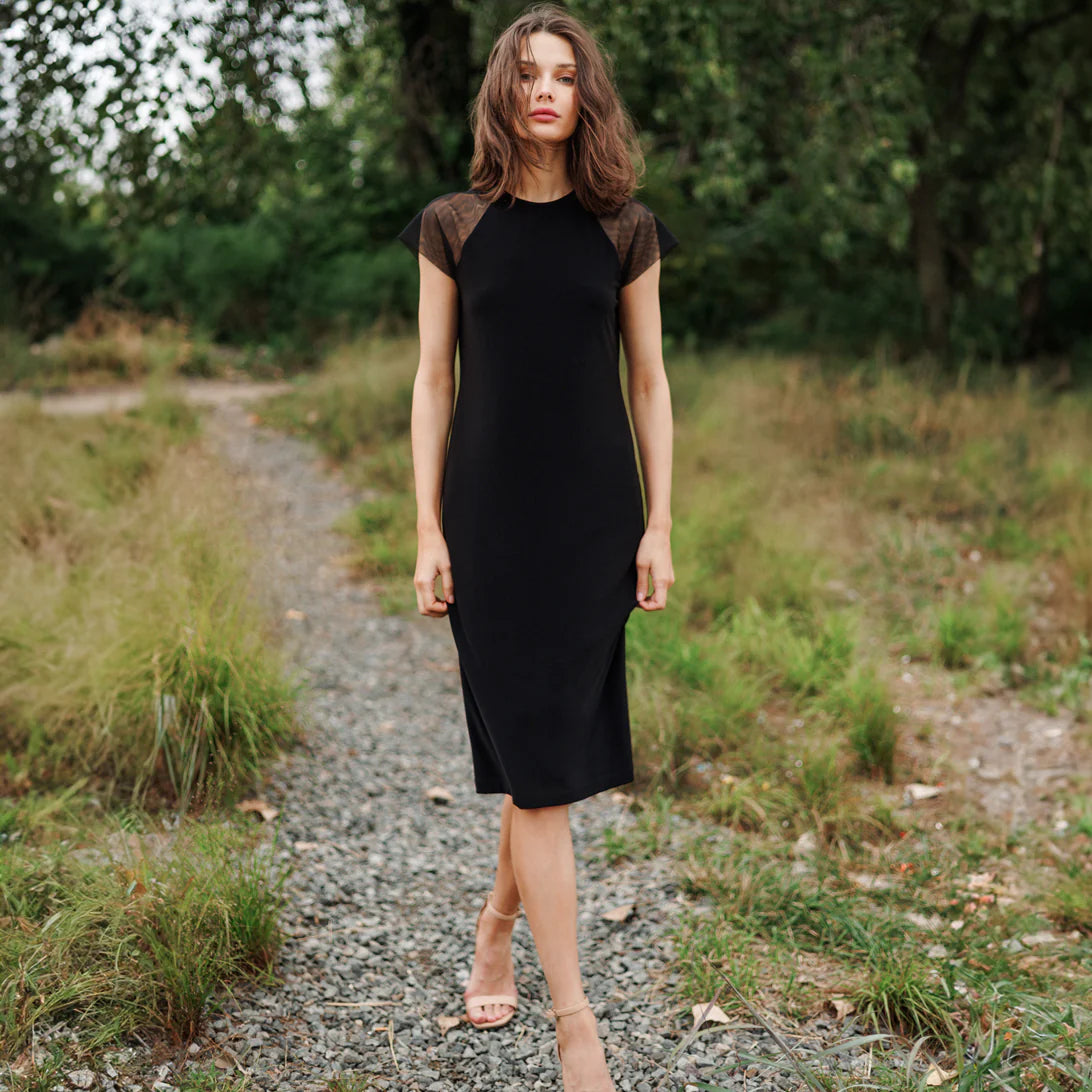 Woman in a black dress standing on a gravel path with greenery around