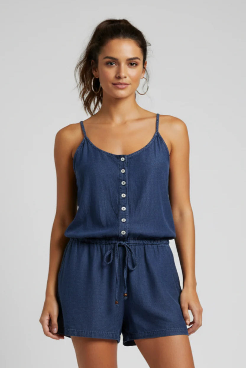 Woman wearing a blue romper with button details on a plain background