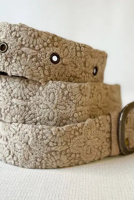 Beige lace belt with a metal buckle on a light background