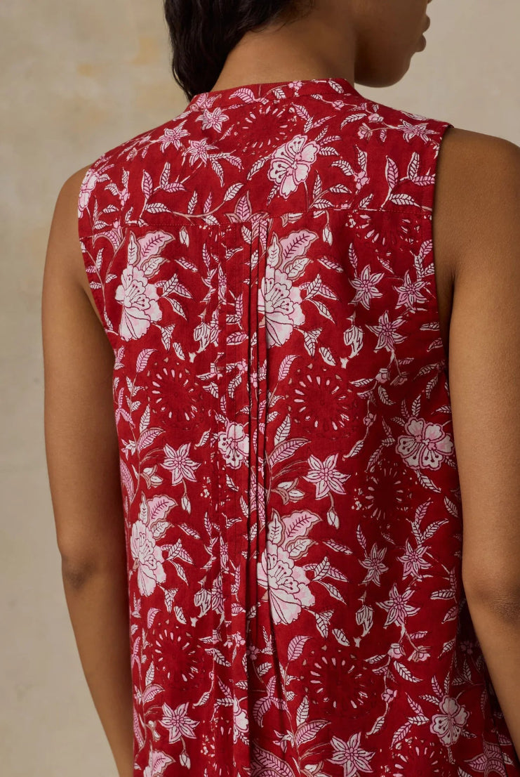 Red sleeveless top with white floral pattern worn by a person against a beige background