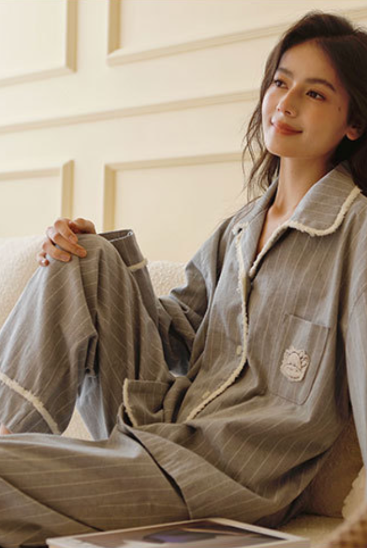 Woman lounging in the grey flannel pajama set on a cream sofa