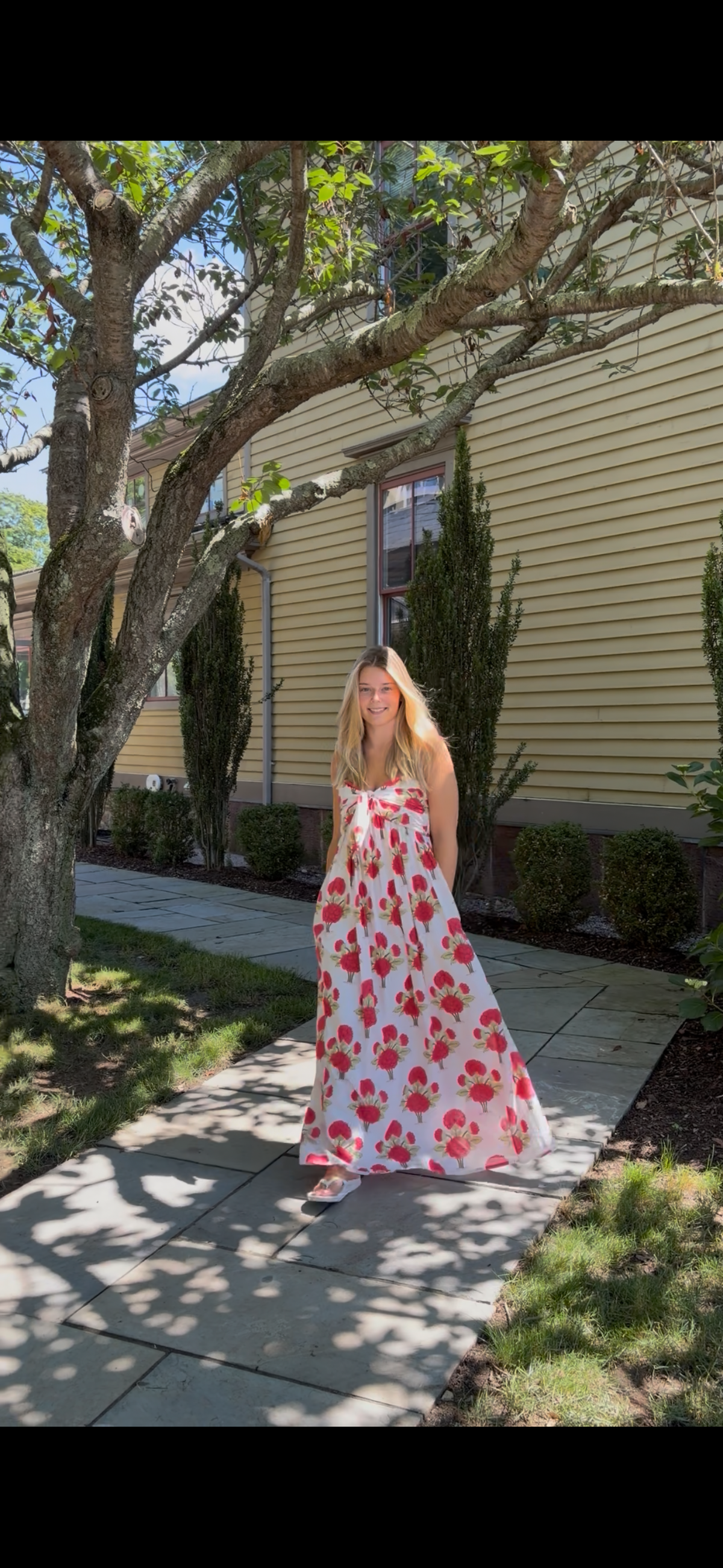 Faherty Voile Alexi Dress in Bloom Poem white with red and green floral print, flowing A-line maxi worn outdoors, front view