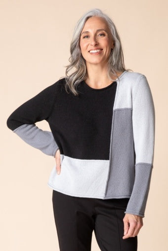 Woman wearing the Habitat Yin Yang Block Party Sweater in Mist, black, grey and pale grey color-block crewneck with black pants