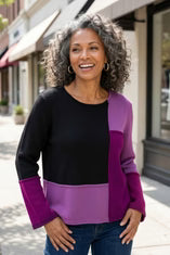 Woman wearing the Habitat Yin Yang Block Party Sweater in Plum, black, lilac and plum color-block crewneck with jeans