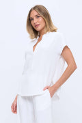 A woman modeling a white short-sleeve top and matching white pants against a plain white studio background.