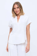 A woman wearing a white short-sleeve collared top and matching white pants, photographed against a plain white studio background.