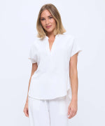 A woman wearing a white short-sleeve collared top and matching white pants, photographed against a plain white studio background.