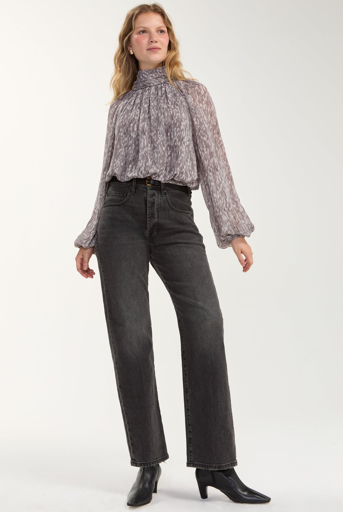 Model wearing the Liverpool grey multi shirred mock neck top tucked into trousers