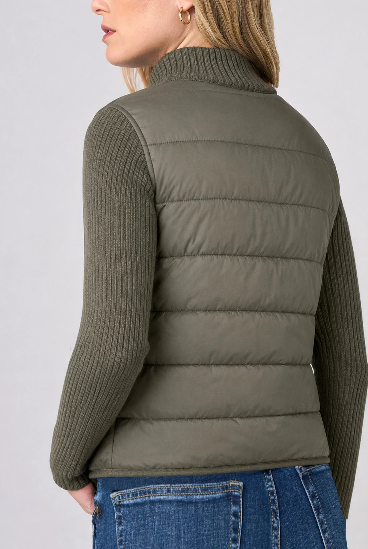 Back view of the Long Sleeve Zip-Front Quilted Sweater Jacket in Heather Olive, showing the quilted puffer back panel and cable-knit sleeves worn with jeans.
