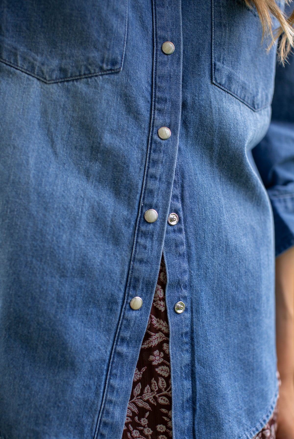 Close-up of the MAREA western shirt in blue showing silver-toned snap buttons and the hem over a patterned skirt