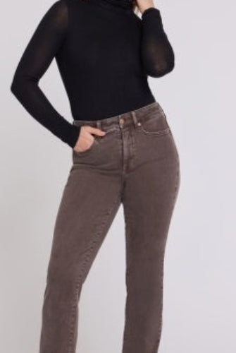 A woman modeling NYDJ High Rise Marilyn Straight petite jeans in Retro Espresso brown wash, paired with a black long-sleeve top and black heeled boots, against a plain light studio background.
