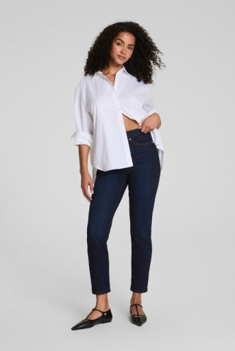 Woman wearing a white shirt and dark blue jeans on a light gray background