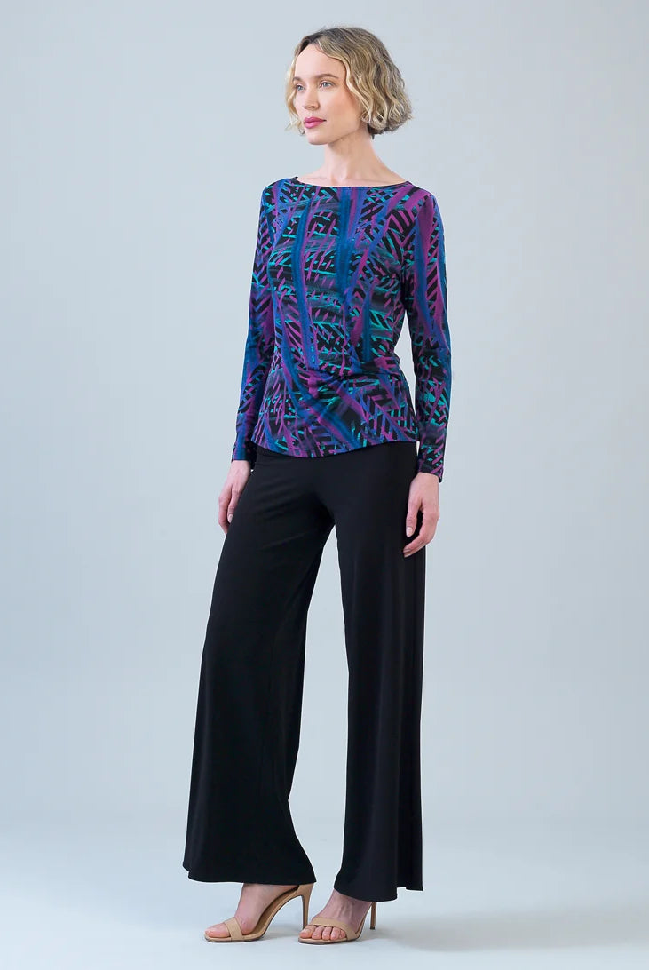 Woman wearing a patterned top and black pants on a plain background