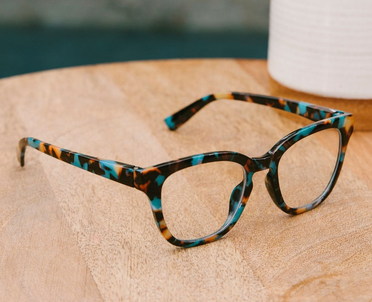 Peepers Betsy cat eye reading glasses in Teal Botanico resting on a wood tabletop