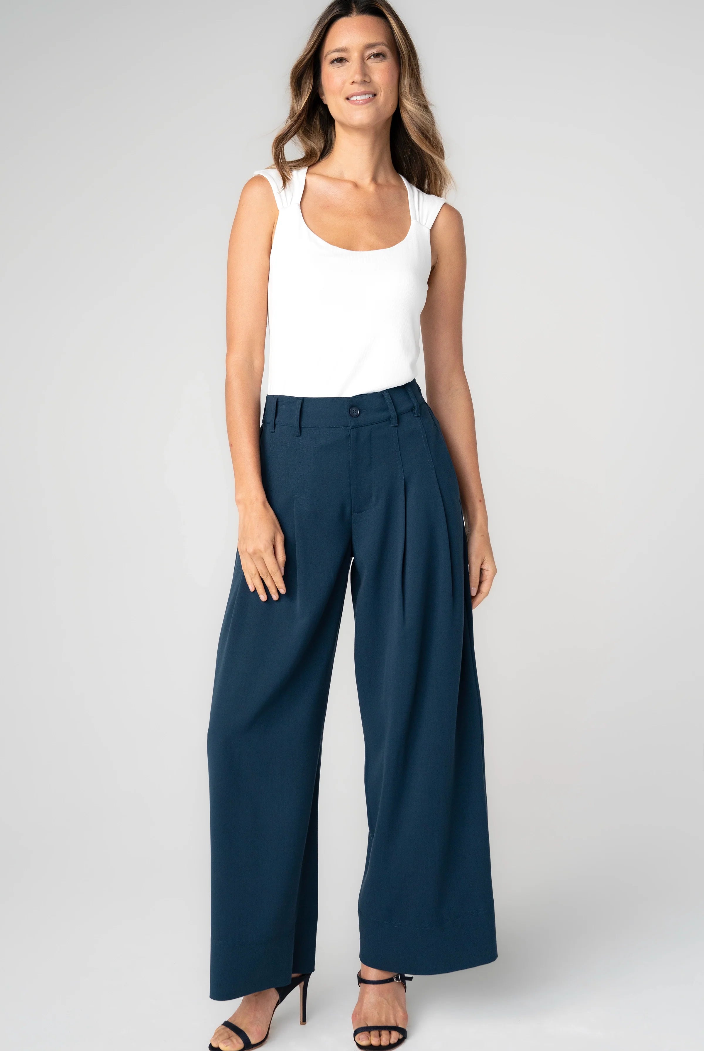 A model wearing pleated wide leg trousers in oxford navy with a high-rise fit.