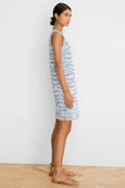 Woman wearing a striped dress standing on a wooden floor with a white wall background