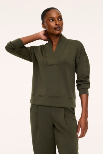 Woman wearing the Spanx AirEssentials V-Neck Long Sleeve Top in Monstera olive green with a wide-collar V-neckline, dropped shoulders, banded cuffs and hem, styled with matching green trousers