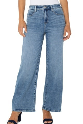 A model wearing a pair of light blue, wide-leg cropped jeans with a faded wash, styled with a white top and navy blue heeled sandals against a plain white background.