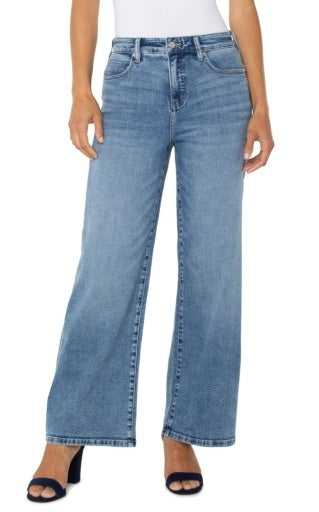 A model wearing a pair of light blue, wide-leg cropped jeans with a faded wash, styled with a white top and navy blue heeled sandals against a plain white background.