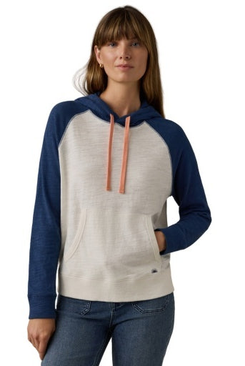 A woman wearing a two-tone raglan hoodie with a cream-colored body and navy blue sleeves and hood, featuring peach drawstrings, paired with blue jeans against a white background.