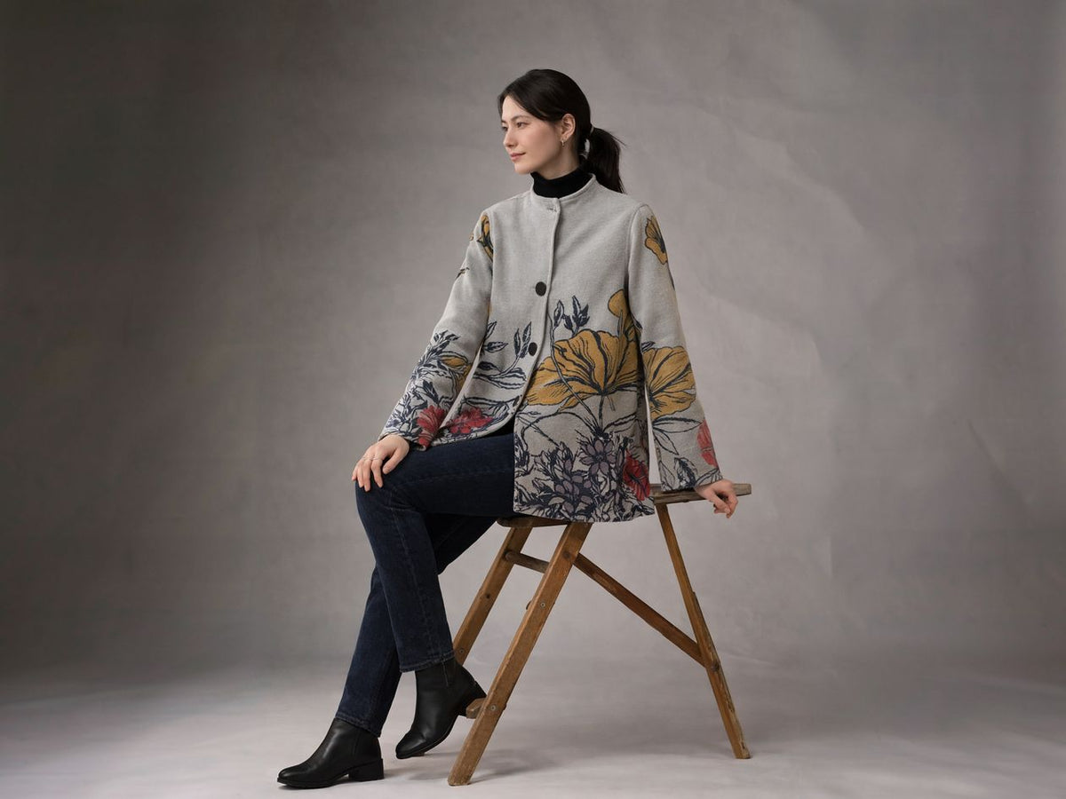 Winding River Floral Fields Asymmetric Travel Coat in dove gray with yellow and blue wildflower print at the hem, worn by a seated model