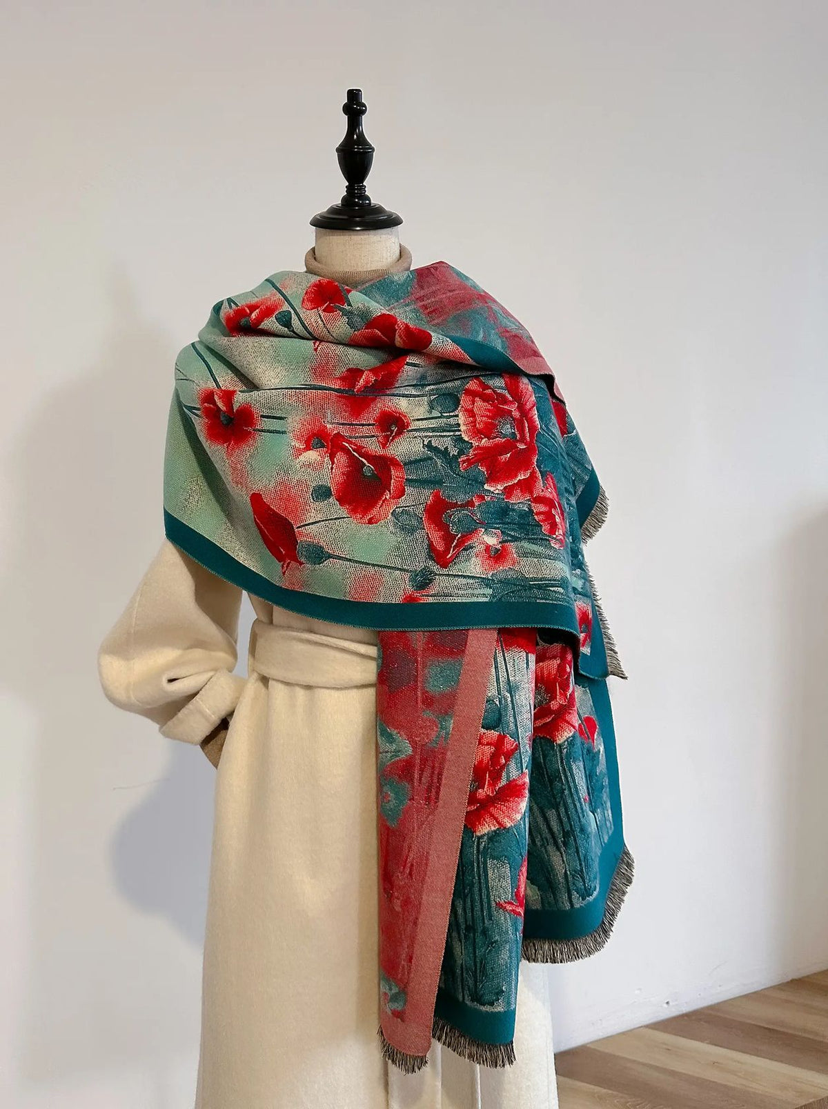 Winding River Poppy Field Reversible Artisan Shawl in turquoise with red poppy print and fringed ends, draped on a dress form over a cream coat