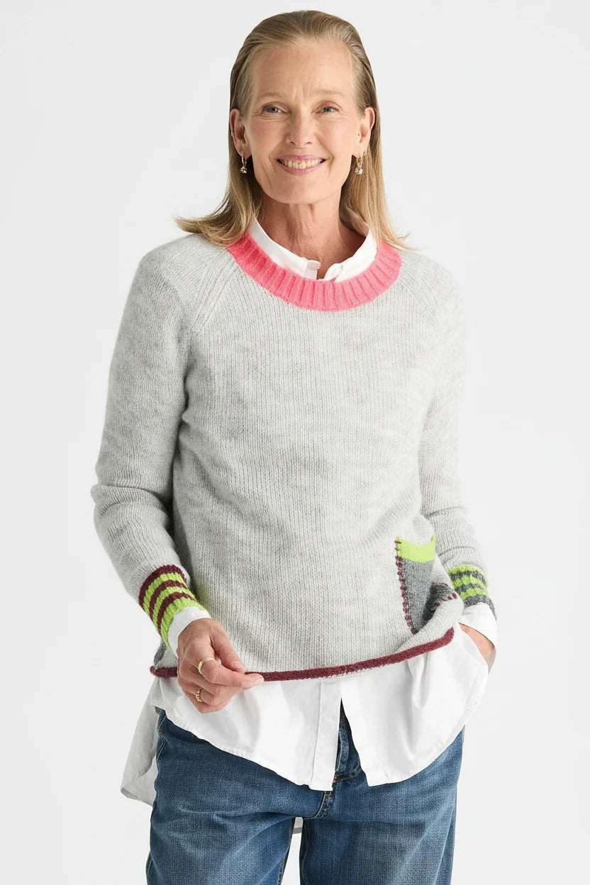 Woman wearing the Zaket & Plover Studio Pop Sweater in Lt Marl, a soft grey knit with a pink crew neck and striped cuffs, layered over a white shirt with blue jeans