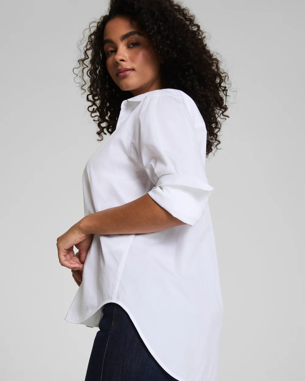 Woman wearing a white blouse with rolled-up sleeves on a plain background