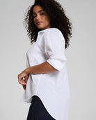 Woman wearing a white blouse with rolled-up sleeves on a plain background