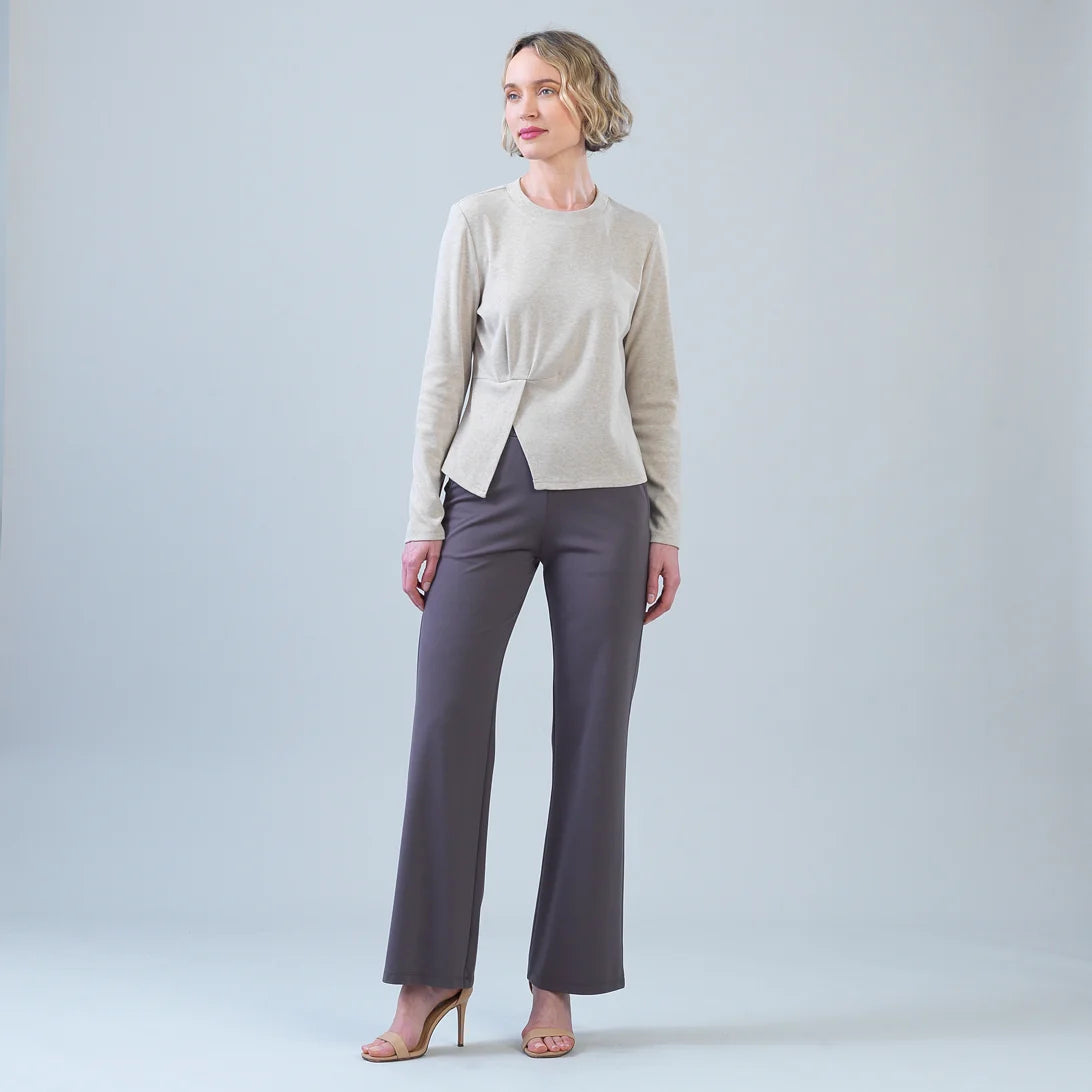 A woman modeling a light beige knit wrap-style cardigan and dark gray wide-leg trousers against a light gray studio background.