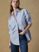 Woman wearing a light blue shirt and dark jeans against a beige background