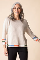 Woman wearing a beige sweater with colorful cuffs and hem on a beige background