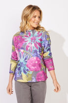 Woman wearing a colorful floral-patterned top against a white background