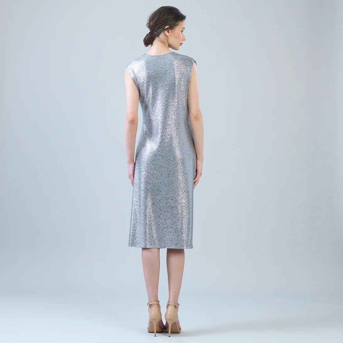 A woman stands with her back to the camera wearing a sleeveless, knee-length silver dress with a subtle speckled texture, paired with beige high heels, against a light gray studio background.