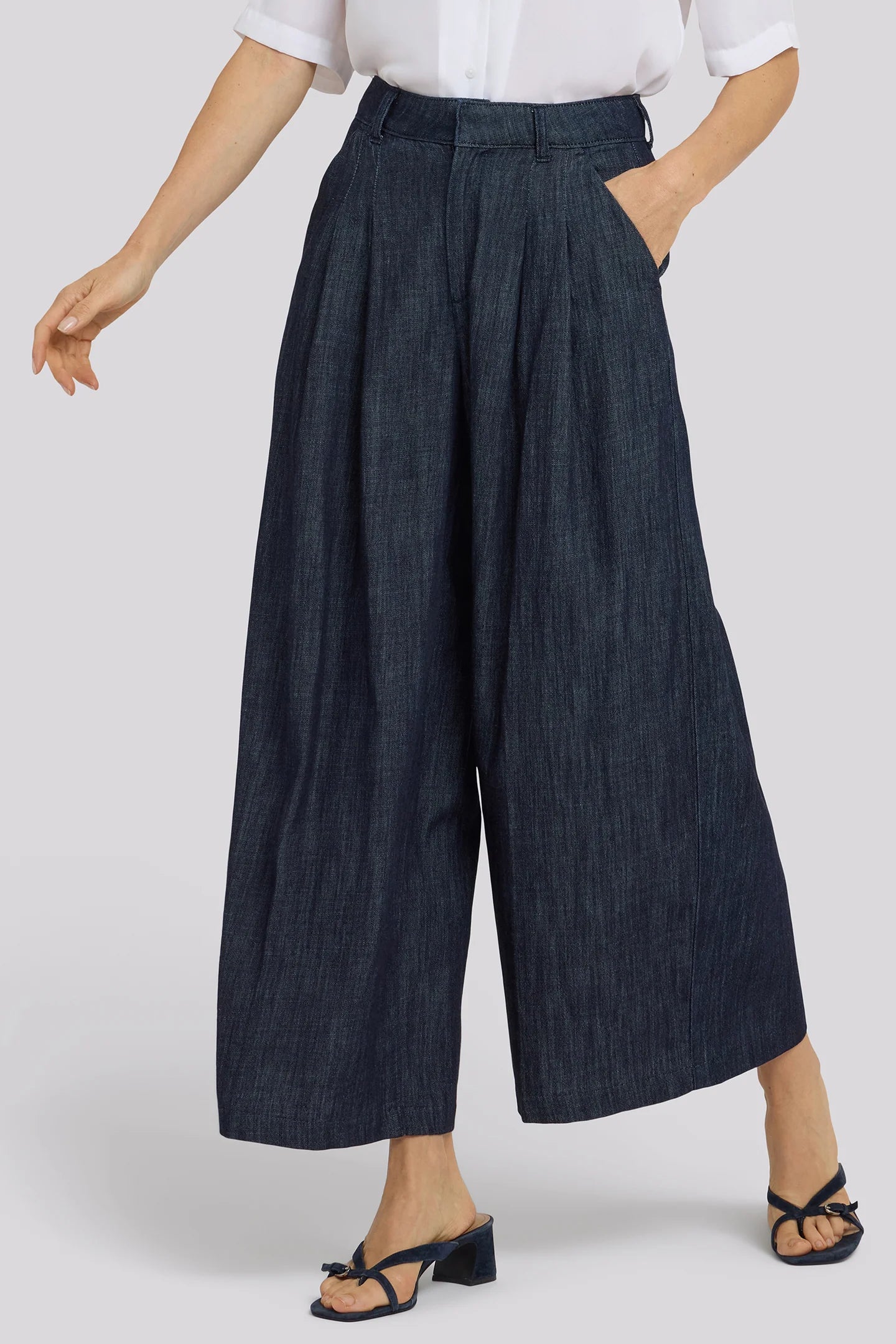 Person wearing dark blue wide-leg pants with a white top on a light gray background