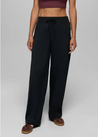A model wearing black wide-leg drawstring pants, styled with a dark purple crop top and brown slip-on shoes, against a neutral gray studio background.