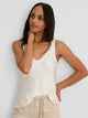 Lace Trim Day Gloss Tank in cream, a woman wearing the sleeveless cream tank with delicate lace trim along the scoop neckline, paired with light beige pants