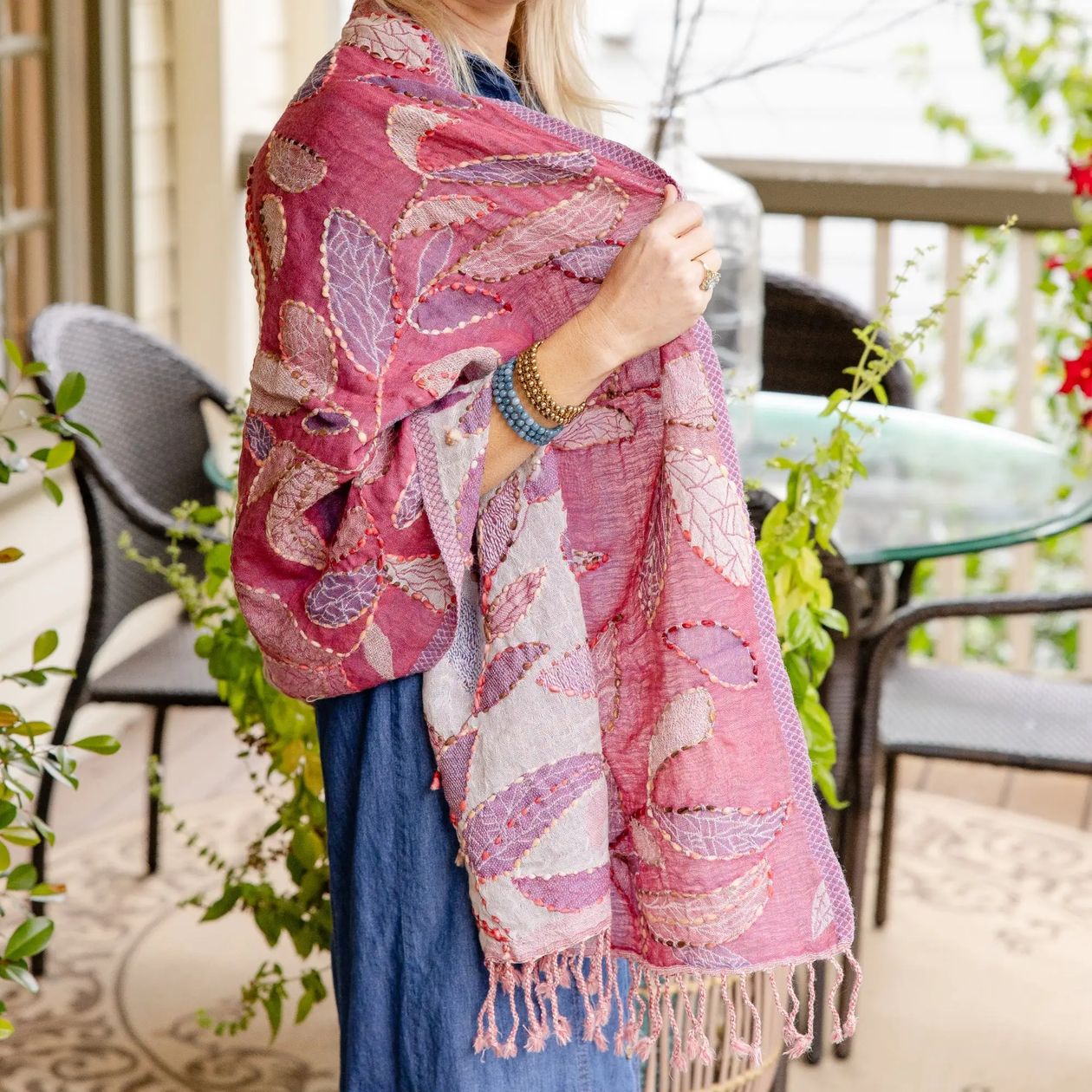 A woman on a balcony wearing a pink and lavender leaf-patterned shawl with fringe, paired with a blue dress.