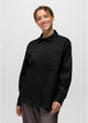 Stretch Zion LS Button Up in Black, woman modeling a black long-sleeve button-up shirt with a chest pocket, paired with dark gray pants, against a light gray studio background