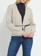 Person wearing a beige cardigan over a black turtleneck and blue jeans on a white background