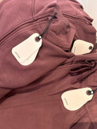 Close-up of mauve-colored Prada zippered clothing with white Prada hang tags attached, showing fabric texture, zipper detail, and drawstring.
